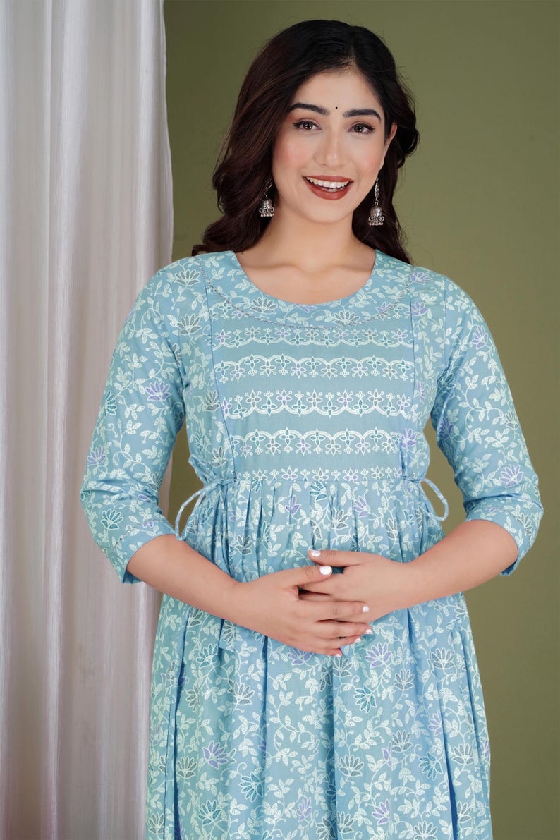K&ouml;nnte beinhalten: Hellblaues Kleid mit floralem Muster und Dreiviertel&auml;rmeln. Das Kleid hat eine betonte Taille und dekorative wei&szlig;e Spitzendetails am Oberteil. Der Stoff hat ein zartes, flie&szlig;endes Aussehen, das sich f&uuml;r Freizeitkleidung eignet.