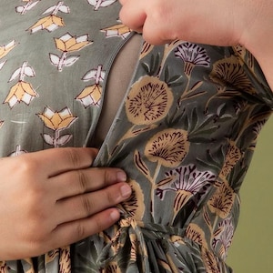 May include: A grey floral print nursing dress with yellow and purple accents. The dress has a wrap design and a tie at the waist. The floral pattern includes stylized flowers and leaves.