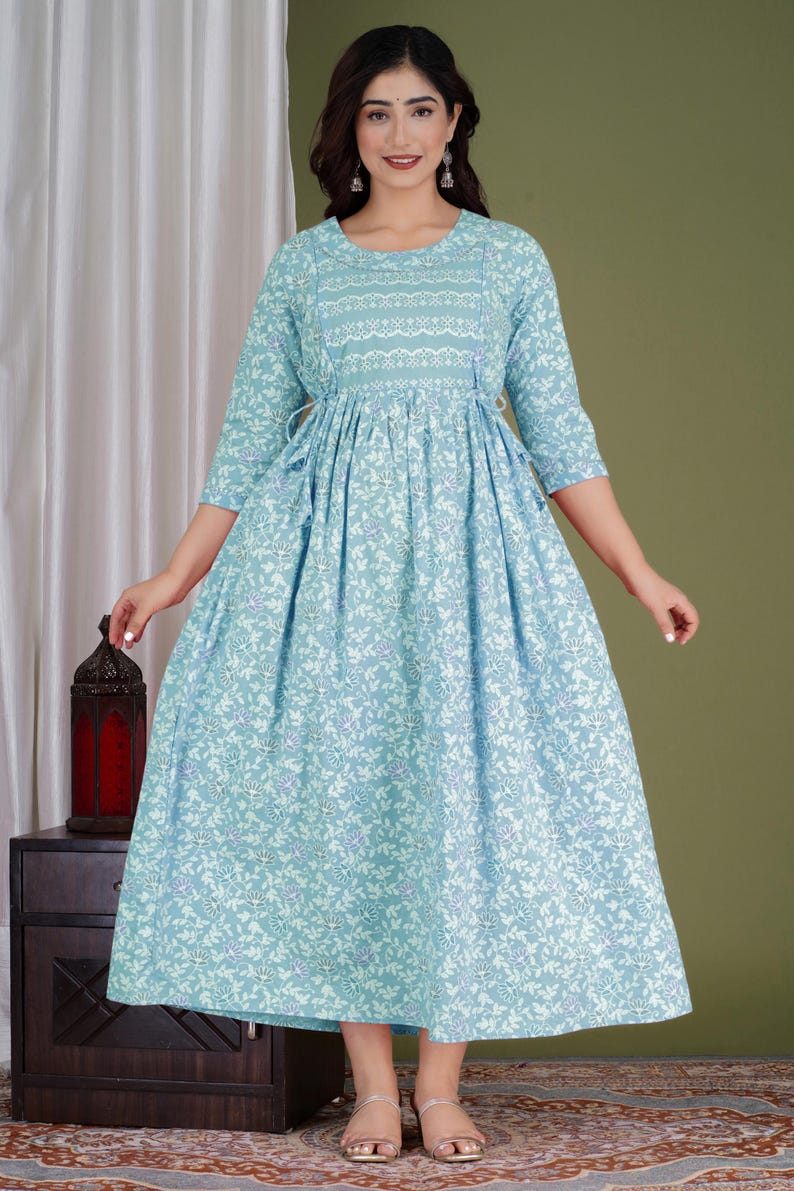 K&ouml;nnte beinhalten: Hellblaues Kleid mit floralem Druck, Dreiviertel&auml;rmeln und rundem Ausschnitt. Das Kleid hat eine betonte Taille und einen flie&szlig;enden Rock. Der Stoff hat ein zartes Blumenmuster in Wei&szlig; und Lila. Das Kleid ist f&uuml;r Freizeitkleidung geeignet.