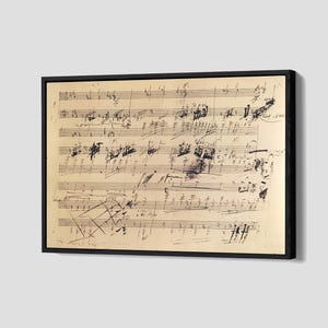 May include: A framed piece of sheet music featuring handwritten musical notation. The paper has a vintage, aged look with black ink markings. The frame is black, and the artwork is set against a light grey backdrop.