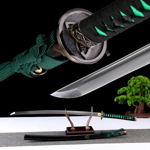 Pode incluir: Uma espada katana japonesa com lâmina prateada e cabo preto com detalhes verdes. A espada é exibida com sua bainha preta e um suporte decorativo. A lâmina tem aproximadamente 76 cm de comprimento.