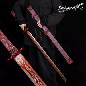 May include: A sword with a red blade featuring intricate patterns and a matching red scabbard with detailed engravings. The sword includes a black tassel and the text Bushidocrafts23 is visible in the upper right corner of the image.