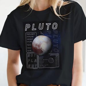 Może przedstawiać: Czarny t-shirt z krótkim rękawem z grafiką planety Pluton. Wzór zawiera napis PLUTO oraz NOT A PLANET, a także tabele z danymi naukowymi dotyczącymi odległości, powierzchni, temperatury, masy, promienia, gęstości oraz objętości planety.