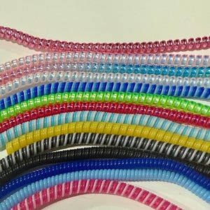 以下が含まれることがあります： カラフルなスパイラル状のケーブルプロテクターのコレクション。プロテクターは、ピンク、ブルー、グリーン、イエロー、ブラックなど、さまざまな色があります。各プロテクターはコイル状のデザインで、充電ケーブルやコードを保護します。