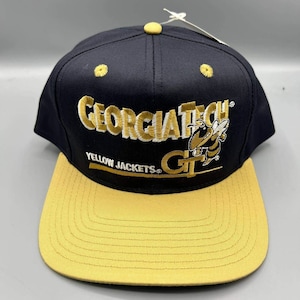 May include: Black and yellow baseball cap with the text "GEORGIA TECH YELLOW JACKETS" embroidered in gold. The cap has a yellow brim and a yellow button on top. A stylized yellow jacket bee logo is also embroidered on the side.