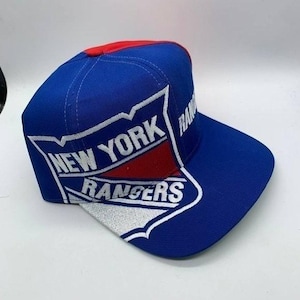 May include: A blue baseball cap with a red top and a white and red logo that says "NEW YORK RANGERS". The cap has a flat peak and is made of a durable fabric.