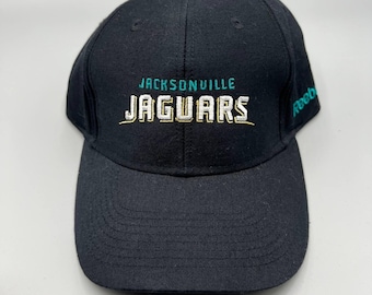 May include: Black baseball cap featuring the text "JACKSONVILLE JAGUARS" in teal and gold embroidery. The Reebok logo is embroidered on the side. The cap has a curved brim and a structured crown.