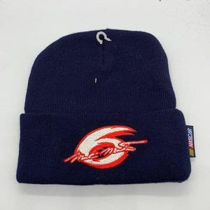Puede incluir: Gorro de punto azul marino con un logotipo bordado en blanco y rojo. El gorro tiene un borde doblado y una pequeña etiqueta con la palabra "NASCAR" en el lateral. Un pequeño diseño blanco está en la parte superior del gorro.