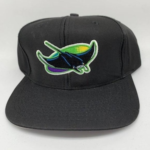 Peut inclure: Casquette de baseball noire avec un écusson brodé coloré d'une raie manta. L'écusson comprend du vert, du jaune, du violet et du noir. La casquette a une visière plate et une couronne structurée.