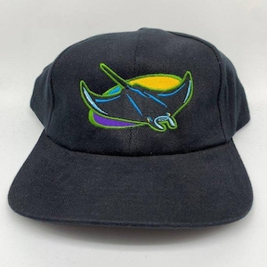 Op de afbeelding: Zwarte baseballcap met een platte klep. De cap heeft een geborduurd ontwerp van een gestileerde manta rog in geel, blauw, groen en paars. De cap is gemaakt van een duurzame stof.
