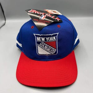 Könnte beinhalten: Eine blau-rote Baseballkappe mit dem Logo der New York Rangers. Die Kappe hat einen roten Schirm und eine blaue Krone, mit dem Logo des Teams in Weiß, Rot und Blau. Das Etikett lautet "Backtalk by Twins Enterprise Boston MA."