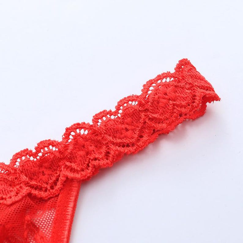 May include: Close-up of red lingerie with delicate lace trim. The lace is scalloped and detailed, adding a touch of elegance. The fabric appears soft and sheer, with a focus on the intricate design and texture.