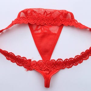 May include: Red thong underwear with delicate lace trim. The thong features a V-shaped front panel and a sheer mesh upper section. The edges are adorned with a scalloped lace design, adding a touch of elegance to the lingerie.