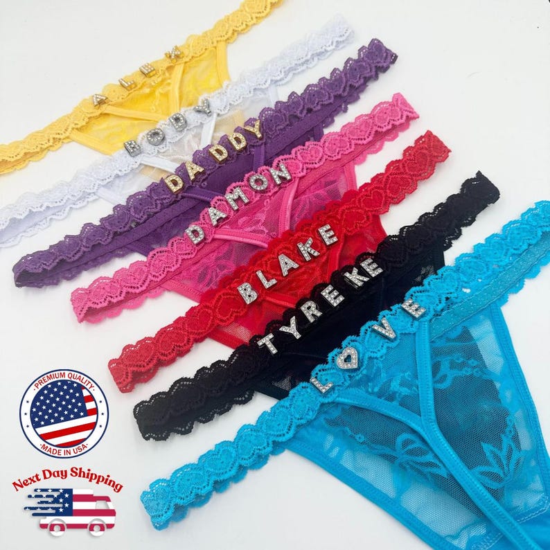 May include: A collection of colorful thong underwear with rhinestone embellishments spelling out names and the word "LOVE". The thongs are in yellow, white, purple, pink, red, black, and blue. Each thong has a lace trim.