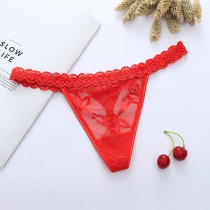 May include: Red lace thong underwear with a floral pattern. The underwear has a scalloped lace trim along the waistband. Two cherries are visible in the image.