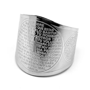 Könnte beinhalten: Ein breiter, silberfarbener Ring mit eingraviertem Text und einem Kreuzdesign. Der Ring hat eine gebogene Form und ist mit religiösem Text beschriftet. Der Ring besteht aus einem glänzenden, metallischen Material.