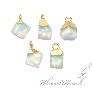 May include: Five opal gemstone pendants with gold-coloured caps and loops. The opals have a milky white and iridescent appearance. The pendants are irregularly shaped, with a polished finish. The text "Bliss & Bezel" is written in cursive at the bottom.