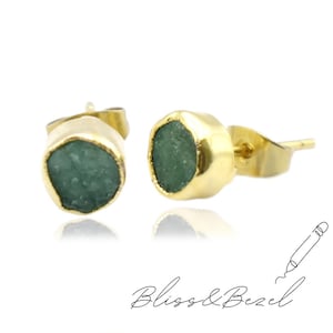 Puede incluir: Un par de pendientes de botón dorados, cada uno con una piedra preciosa verde-azulado en bruto. Los pendientes tienen un engaste biselado y un cierre de poste. La marca "Bliss & Bezel" está escrita en cursiva debajo.