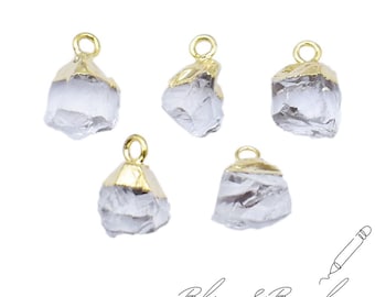 May include: Five clear quartz crystal pendants with gold-colored caps and loops. The raw, irregular quartz pieces are partially encased in gold-toned metal. The pendants are arranged on a white background. The text "Bliss & Bezel" is written in cursive.