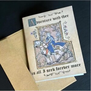 May include: A greeting card with a medieval illustration of a person on horseback, wearing blue and riding a white horse. The card reads "Adventure with thee is all I seek forever more" in black script. The card is tan and comes with a matching envelope.