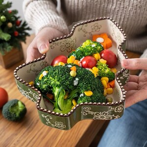 Pode incluir: Um prato de servir de cerâmica verde em forma de folha cheio de brócolis, tomates e milho. O prato tem um padrão floral decorativo e uma borda marrom. O prato está sendo segurado por uma pessoa.