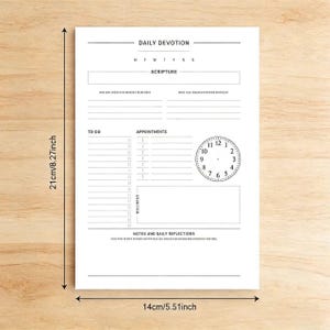 Op de afbeelding: Een witte dagelijkse devotieplanner met zwarte tekst en een klokafbeelding. De planner bevat secties voor schrift, takenlijsten, afspraken en notities. De planner is 21 cm hoog en 14 cm breed.