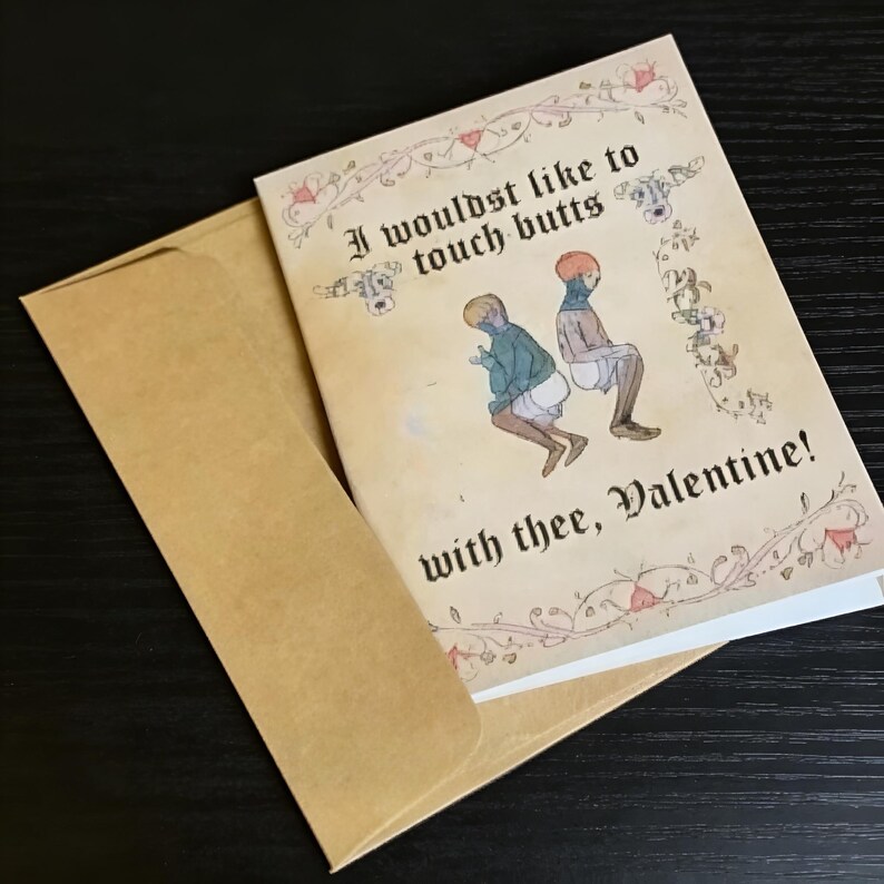 May include: A Valentine's Day card with a medieval illustration of two figures with the text "I wouldst like to touch butts with thee, Valentine!" The card is inside a brown envelope, set against a dark surface.