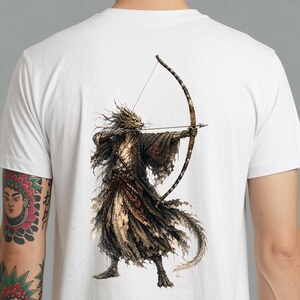以下が含まれることがあります： 背面に詳細なグラフィックプリントが施された白いTシャツ。イラストは、爬虫類のような特徴を持つ人型の生き物を描いており、ぼろぼろの暗いローブを身にまとい、矢をつがえた大きな湾曲した弓を構えています。