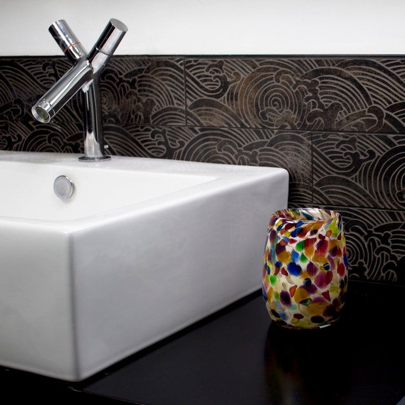 May include: A white porcelain bathroom sink with a chrome faucet and a colorful glass vase on a black countertop.
