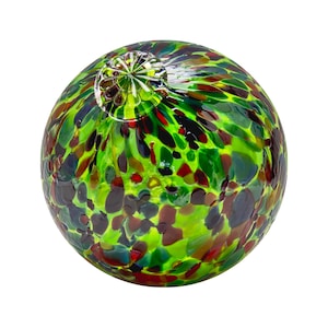 May include: A green glass ball with a speckled pattern of red, black, and green. The ball has a smooth, shiny surface.