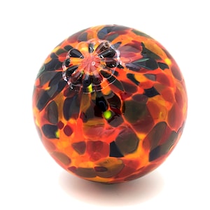 May include: A round, orange, red, and black glass orb with a textured surface. The orb has a small opening at the top.