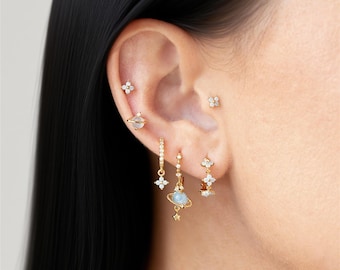 Könnte beinhalten: Nahaufnahme eines Ohrs, das mit mehreren goldenen Ohrringen geschmückt ist. Die Ohrringe umfassen kleine Ohrstecker, Creolen und hängende Designs mit weißen Edelsteinen und himmlischen Charms.
