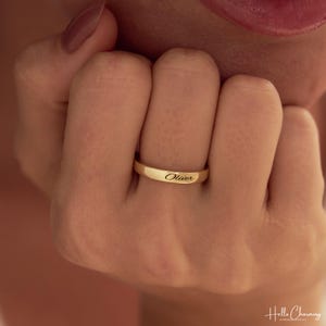 Peut inclure: Une bague anneau en or poli portant le prénom Oliver gravé dans une police cursive classique sur la surface extérieure. La bague présente un profil lisse et arrondi ainsi qu'une largeur constante, offrant un design épuré et brillant.