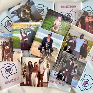K&ouml;nnte beinhalten: Eine Sammlung quadratischer Magnete mit verschiedenen gedruckten Fotos von Menschen, Hunden und Kindern sowie hellblauen Magneten, die ein Kamerasymbol mit einem Herz und den Text Kind Keeps Co. auf einer wei&szlig;en Oberfl&auml;che zeigen.