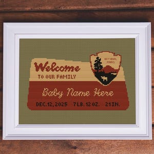 May include: A framed cross-stitch design with the text "Welcome to our family" and "Baby Name Here." The design includes a National Parks emblem and baby's birth details: December 12, 2025, 7 lbs 12 oz, and 21 inches.