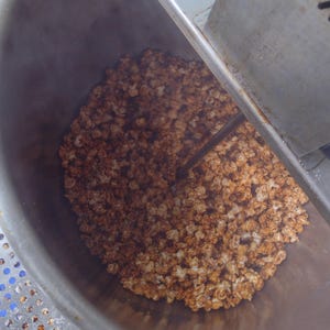 May include: A close-up shot of a large, stainless steel popcorn machine filled with freshly made caramel popcorn. The popcorn is a mix of golden brown and light tan colors, with a slightly glossy appearance. The machine's interior is visible, showing the stirring mechanism.