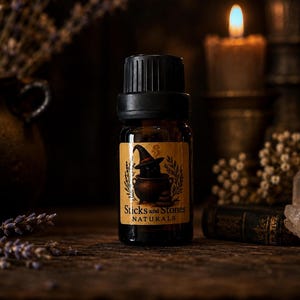 May include: A small amber glass bottle with a black screw-top cap and a tan label. The label features a black cat wearing a pointed hat inside a cauldron, with the text Sticks and Stones NATURALS printed in black lettering below the illustration.