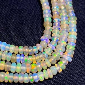 May include: Close-up of several strands of opalescent gemstone beads. The beads are oval-shaped and display a range of colors, including white, blue, green, and yellow. The beads are strung together, creating a necklace or bracelet.