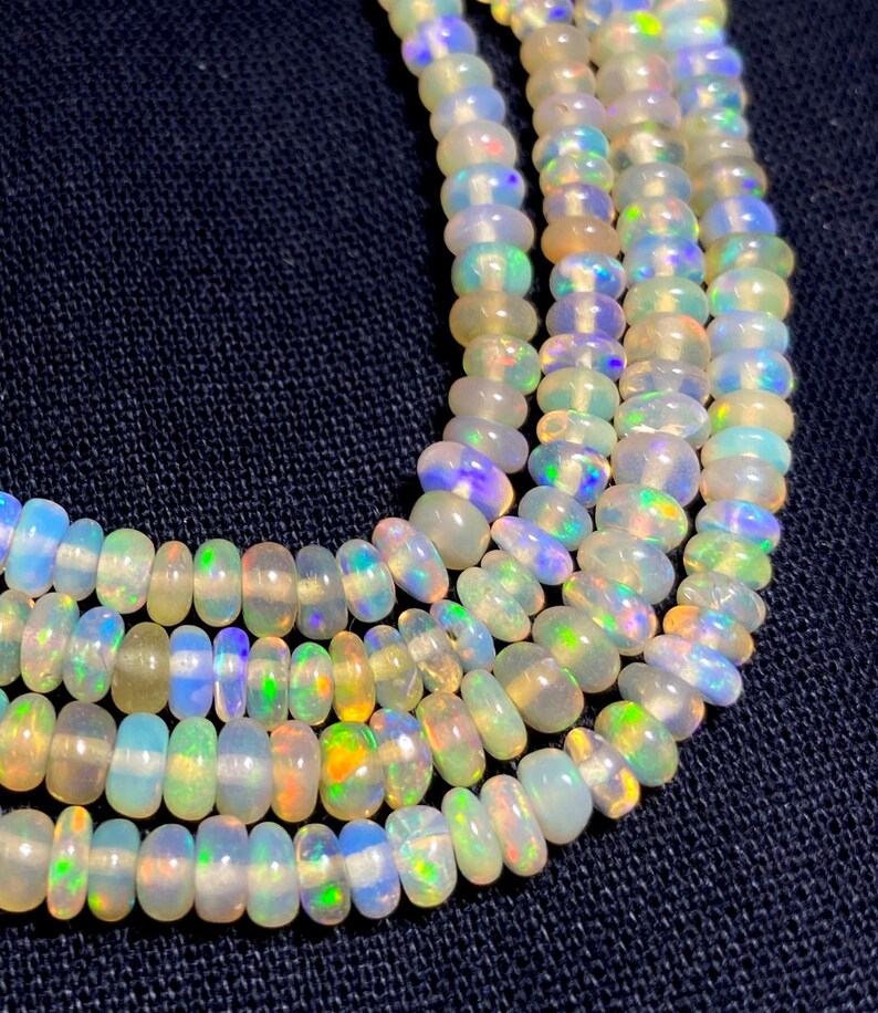 May include: Close-up of several strands of opalescent gemstone beads. The beads are oval-shaped and display a range of colors, including white, blue, green, and yellow. The beads are strung together, creating a necklace or bracelet.