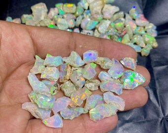 May include: A handful of raw opals, showcasing a variety of shapes and sizes. The opals display a play of color, with flashes of green, blue, and orange. The background features more raw opals.