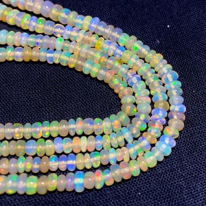 May include: Close-up of several strands of opal beads. The beads are a mix of white, cream, and iridescent colors, with flashes of blue, green, and yellow. The beads are strung together, creating a necklace or bracelet.