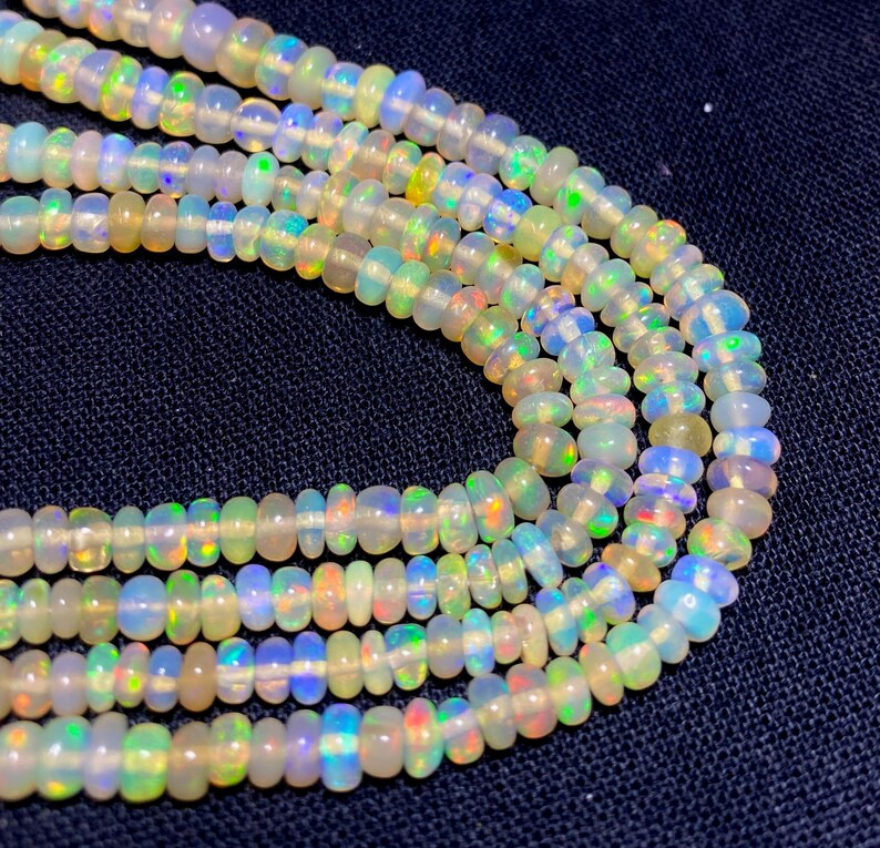 May include: Close-up of several strands of opal beads. The beads are a mix of white, cream, and iridescent colors, with flashes of blue, green, and yellow. The beads are strung together, creating a necklace or bracelet.