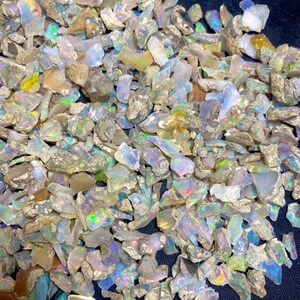 May include: A close-up view of a pile of raw opal gemstones. The opals display a variety of colors, including white, blue, green, and yellow, with iridescent flashes. The rough stones have a natural, unpolished appearance.