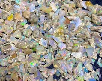May include: A close-up view of a pile of raw opal gemstones. The opals display a variety of colors, including white, blue, green, and yellow, with iridescent flashes. The rough stones have a natural, unpolished appearance.