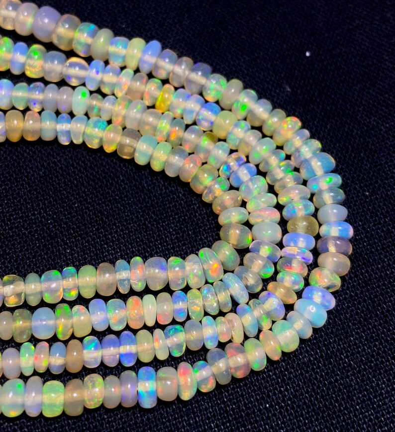 May include: Close-up of several strands of opal beads. The beads are a mix of white, yellow, green, and blue, with iridescent flashes. The beads are strung together, creating a necklace or bracelet.