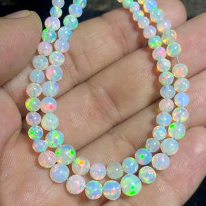 May include: Two strands of iridescent opal beads. The beads are round and vary in size, displaying flashes of color including pink, green, and blue. The opals are strung together, creating a necklace or bracelet.