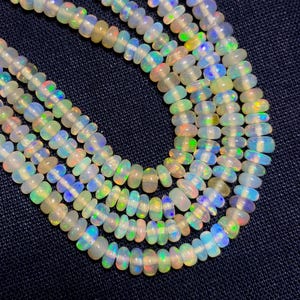 May include: Strands of opalescent beads with iridescent flashes of color. The beads are oval-shaped and strung together, creating a necklace-like appearance. The beads have a milky white base with hints of blue, green, and yellow.