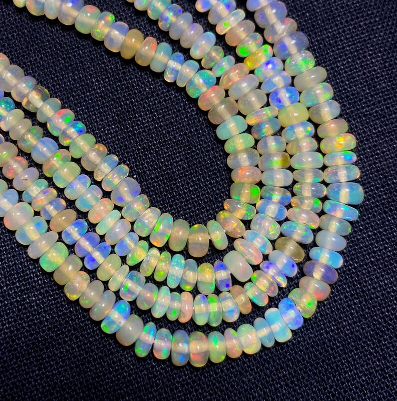 May include: Strands of opalescent beads with iridescent flashes of color. The beads are oval-shaped and strung together, creating a necklace-like appearance. The beads have a milky white base with hints of blue, green, and yellow.