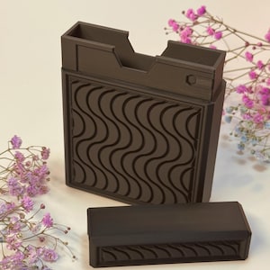 May include: A dark brown, rectangular desk organizer with a wavy pattern on the front. The organizer has a compartment on top and a separate, matching lid. The design is modern and minimalist.