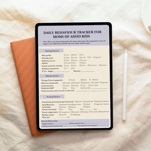 May include: A digital tablet displaying a daily behavior tracker for moms of ADHD kids, with sections for morning, mid-day, and evening check-ins. The tablet rests on a burnt orange notebook, with a white stylus pen nearby.